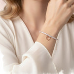 Rose gold tennis bracelet with square crystal stones and dangling open heart charm on a delicate chain.