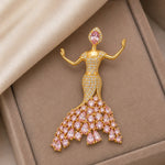 Pink crystal dancer brooch with gold finish and sparkling stones in elegant flowing dress design
