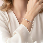 Rose gold tennis bracelet with square crystal stones and dangling open heart charm on a delicate chain.