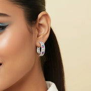 Luxury rainbow crystal hoop earrings with colourful baguette stones and sparkling halo detailing on a polished silver finish.
