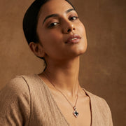 Rose gold clover pendant necklace and matching earrings set with black enamel detailing on a minimal background.
