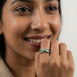 Luxury emerald green crisscross baguette ring with sparkling stone detailing and modern layered band design for women.

